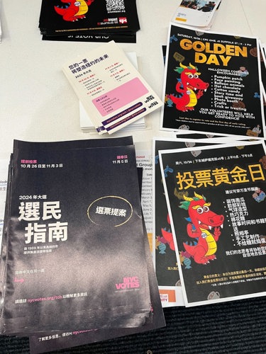 A table of voter guides, palm cards and an illustrated flyer with a dragon promoting Golden Day, in Chinese.